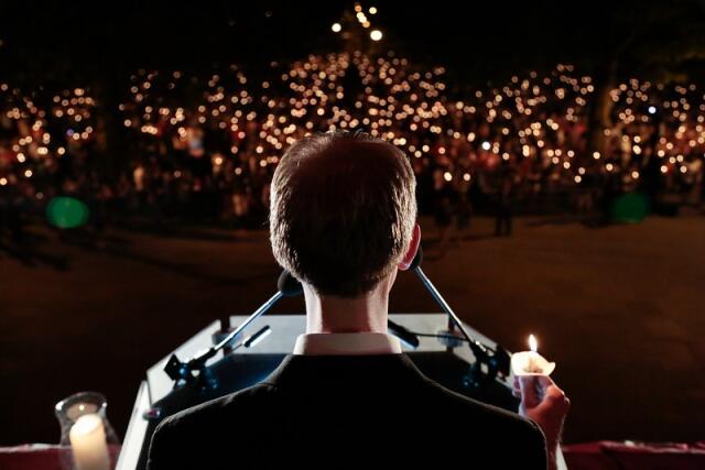 A student at a podium holding a candle in front of a crowd holding up candles.